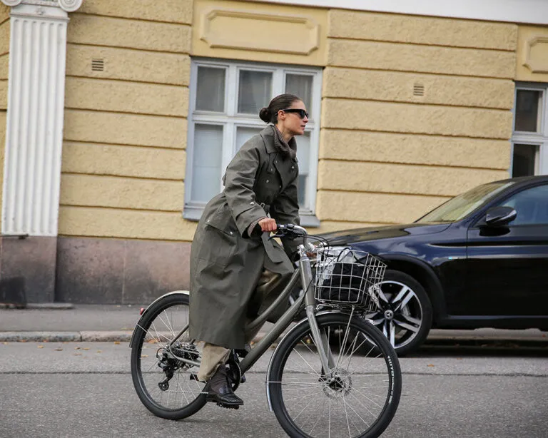Gray Pelago city bike with basket, classic frame; a woman in a coat riding through the city