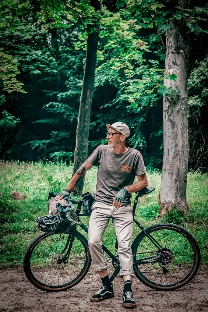 Black Pelago bike with panniers, a man leaning against it, forest in the background