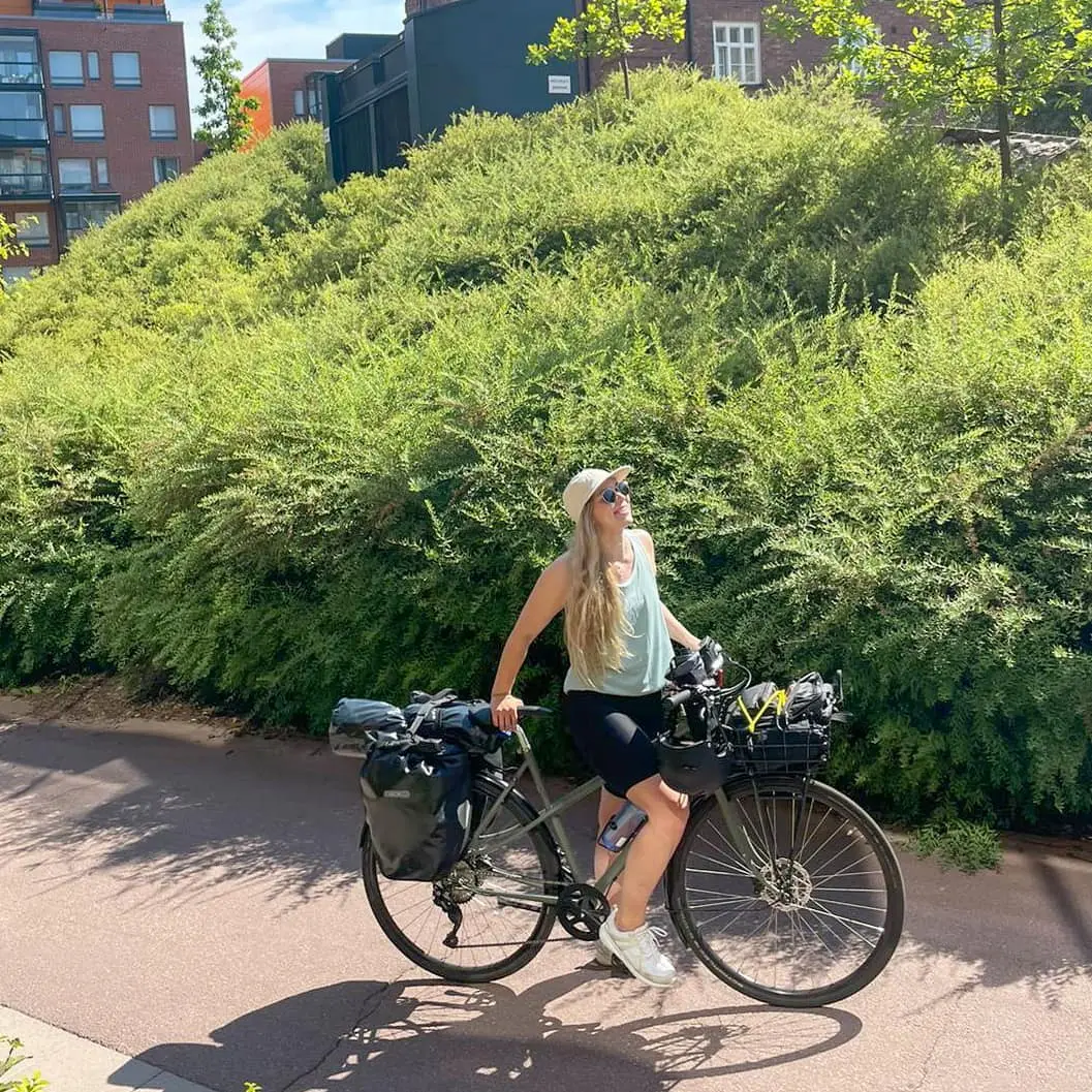 Gray Pelago bike with panniers, smiling cyclist, leafy urban path