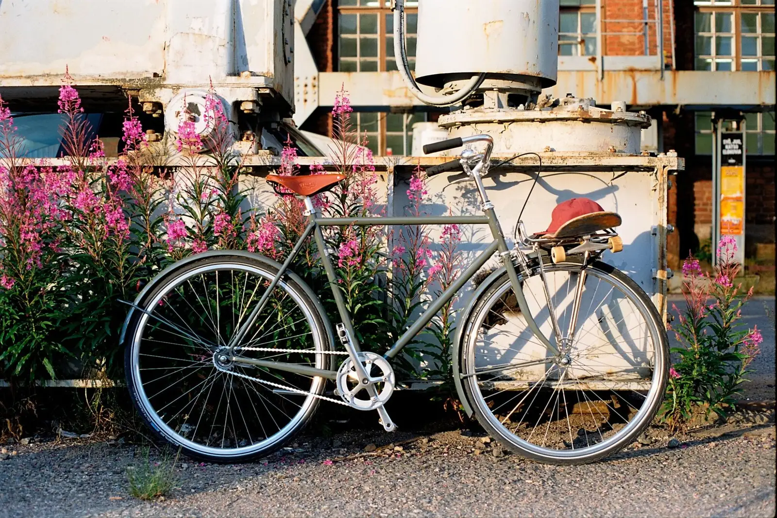 Gray Pelago bike with a classic frame, brown saddle, industrial backdrop, and pink flowers