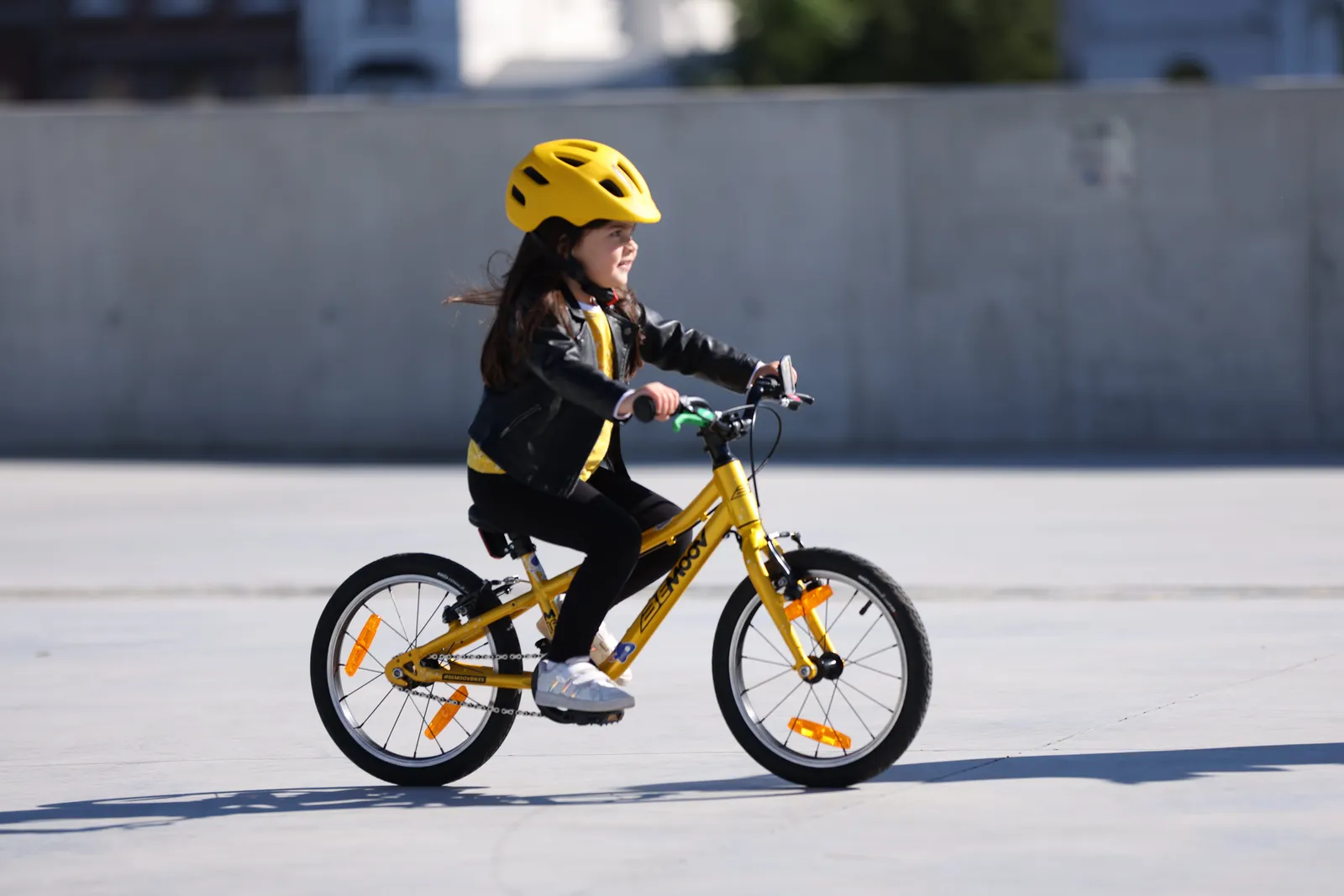 Yellow BeMoov children's bike with a lightweight frame, ridden by a girl wearing a yellow helmet on a concrete surface