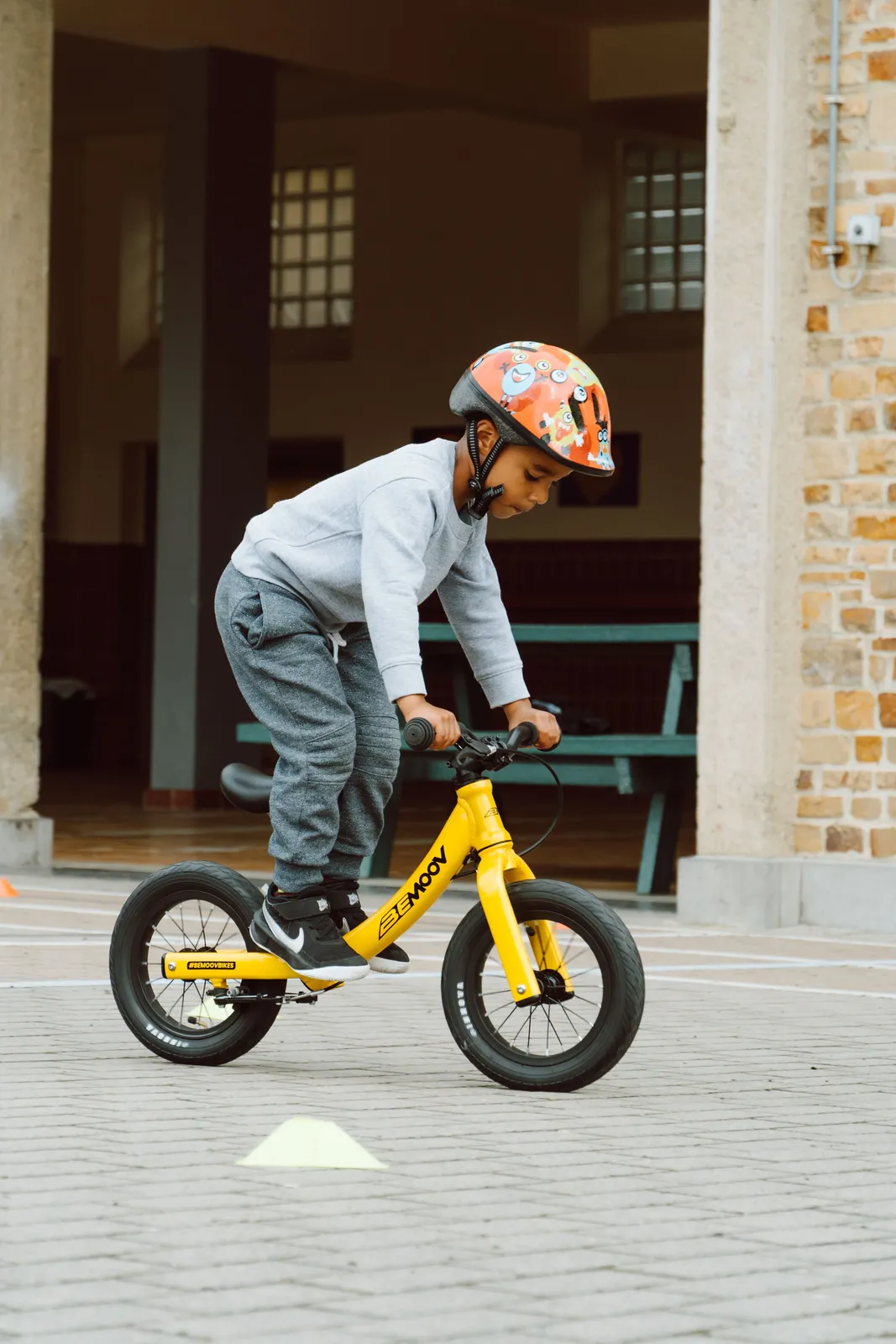 BeMoov yellow children's bike, lightweight frame, front yard, brick wall in the background
