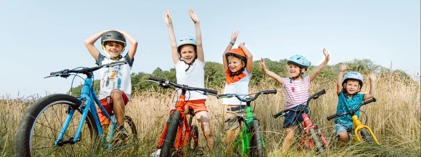 Smiling children riding colorful BeMoov bikes in a sunny field
