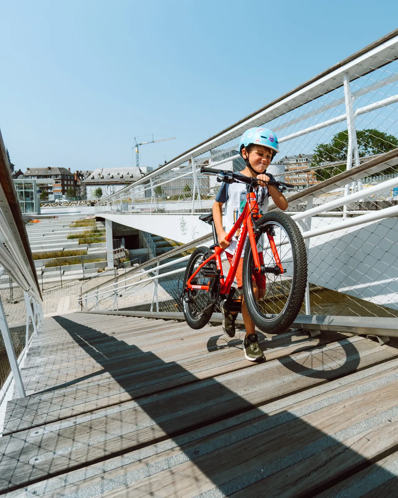 BeMoov red children's bike, lightweight frame, on a wooden walkway, boy wearing a helmet