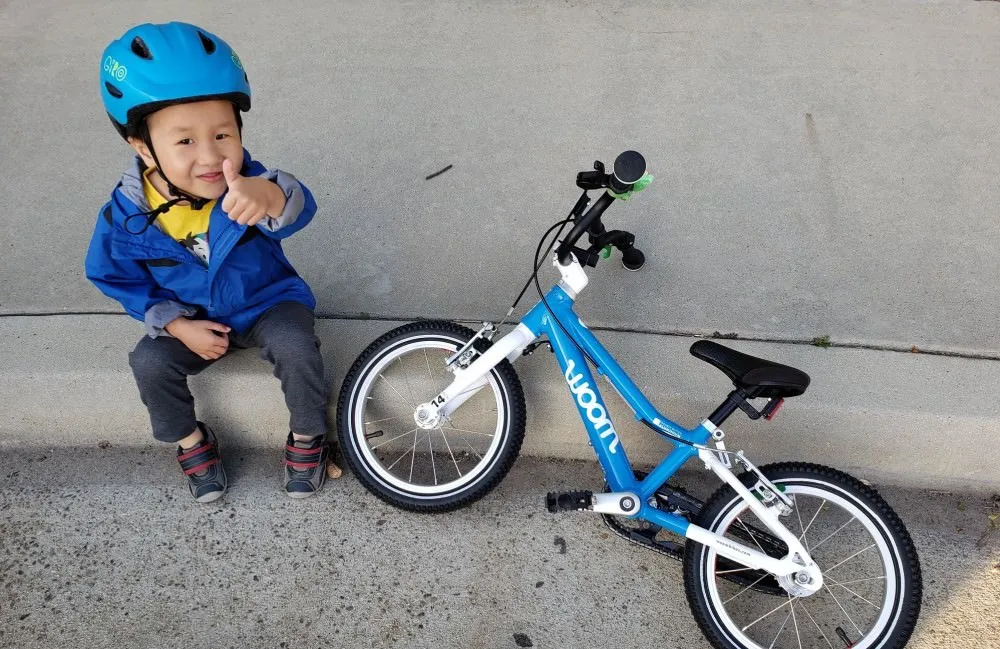 Blue Woom children's bike with matching helmet on a light-colored concrete sidewalk