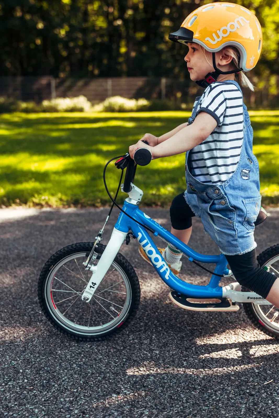 Blue and white Woom children's bike on a sunny path, featuring a lightweight frame and black handlebars