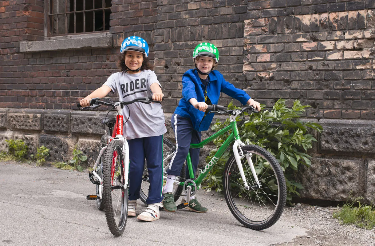 Red and green Woom children's bikes with lightweight frames in front of a brick wall