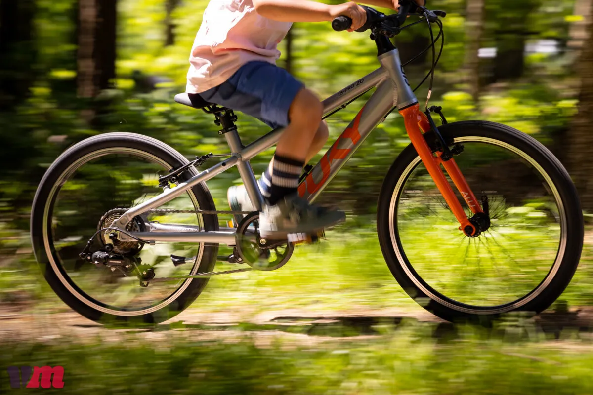 Puky gray and orange children's bike riding on a wooded trail
