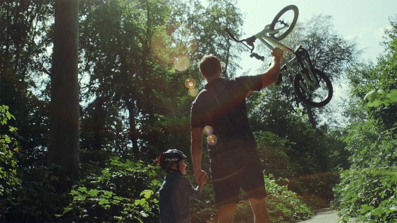 A light green Puky children's bike being picked up by an adult in a forest outdoors