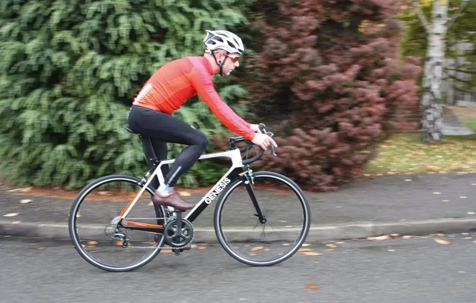Cycliste sur vélo Genesis de route noir et blanc, cadre léger, fond d'arbres et trottoir