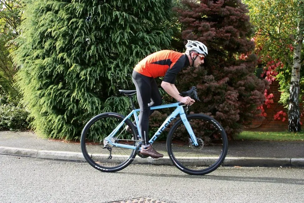 Vélo de route Genesis bleu clair sur une route bordée d'arbres