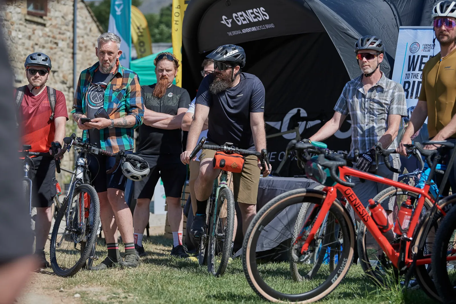 Vélo Genesis rouge avec cadre robuste, cyclistes en arrière-plan, tente de la marque visible