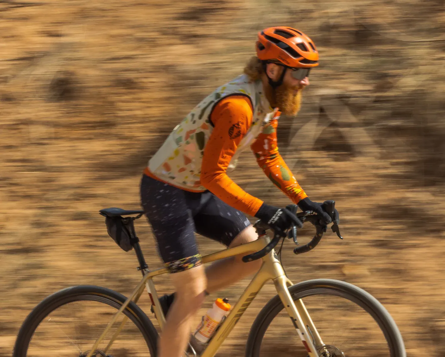 Vélo gravel Salsa beige, cycliste sur chemin terreux, casque orange