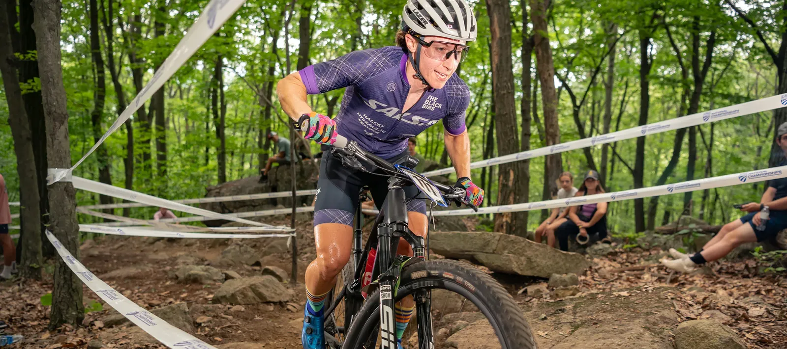 Vélo de course Salsa noir en forêt, cycliste en tenue violette et casque blanc