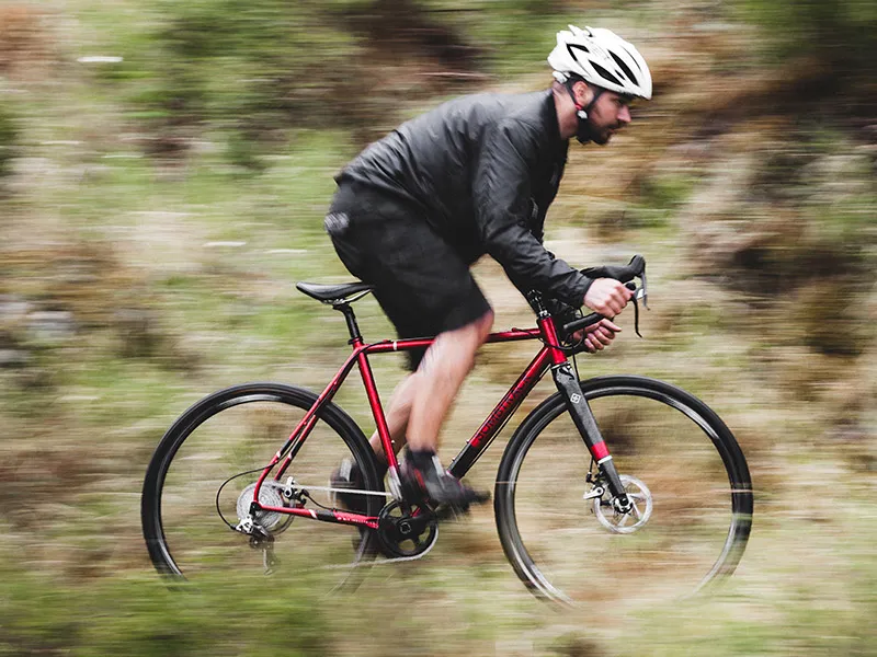 Red Bombtrack road bike with a lightweight frame riding on a natural trail