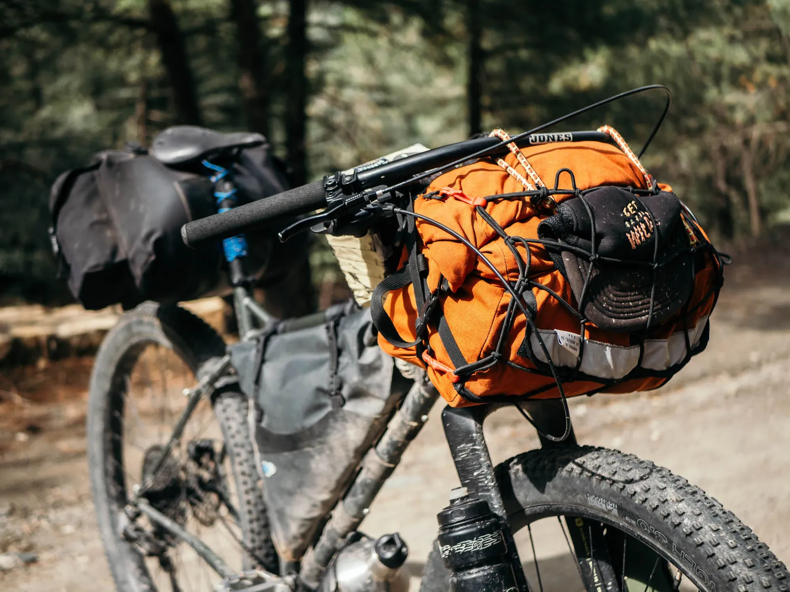 Bombtrack bike loaded for adventure, orange pannier, sturdy frame, forest in the background