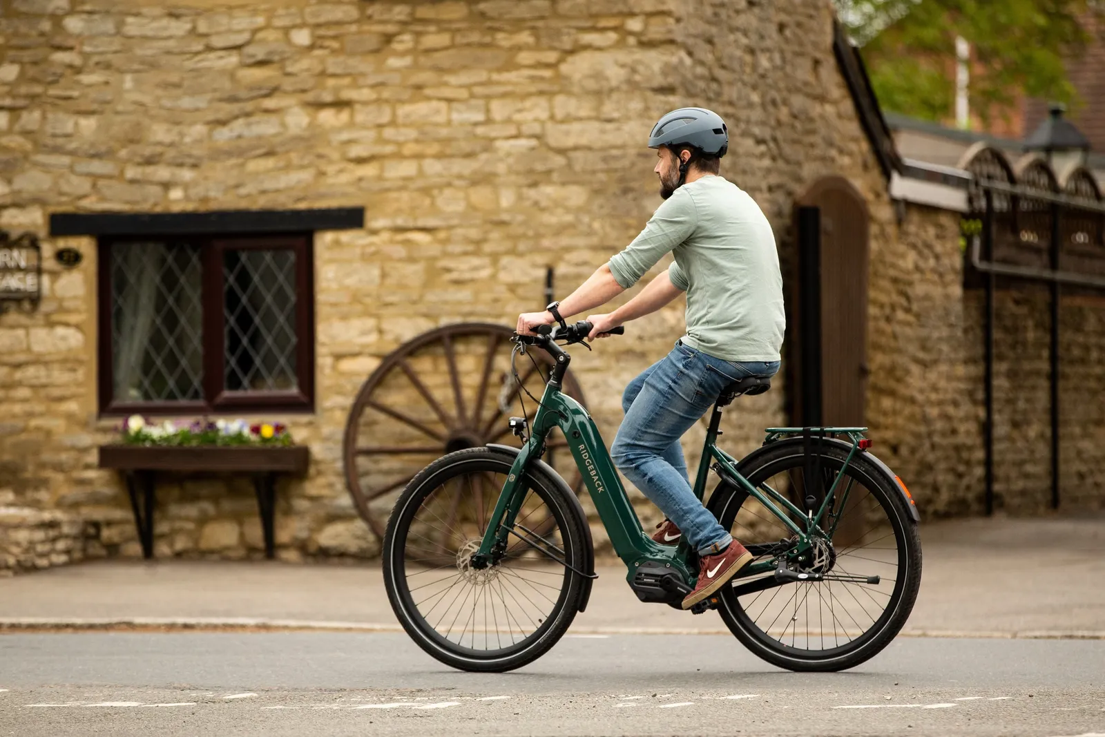 A dark green Ridgeback e-bike with a sturdy frame on a cobblestone street in front of a stone house