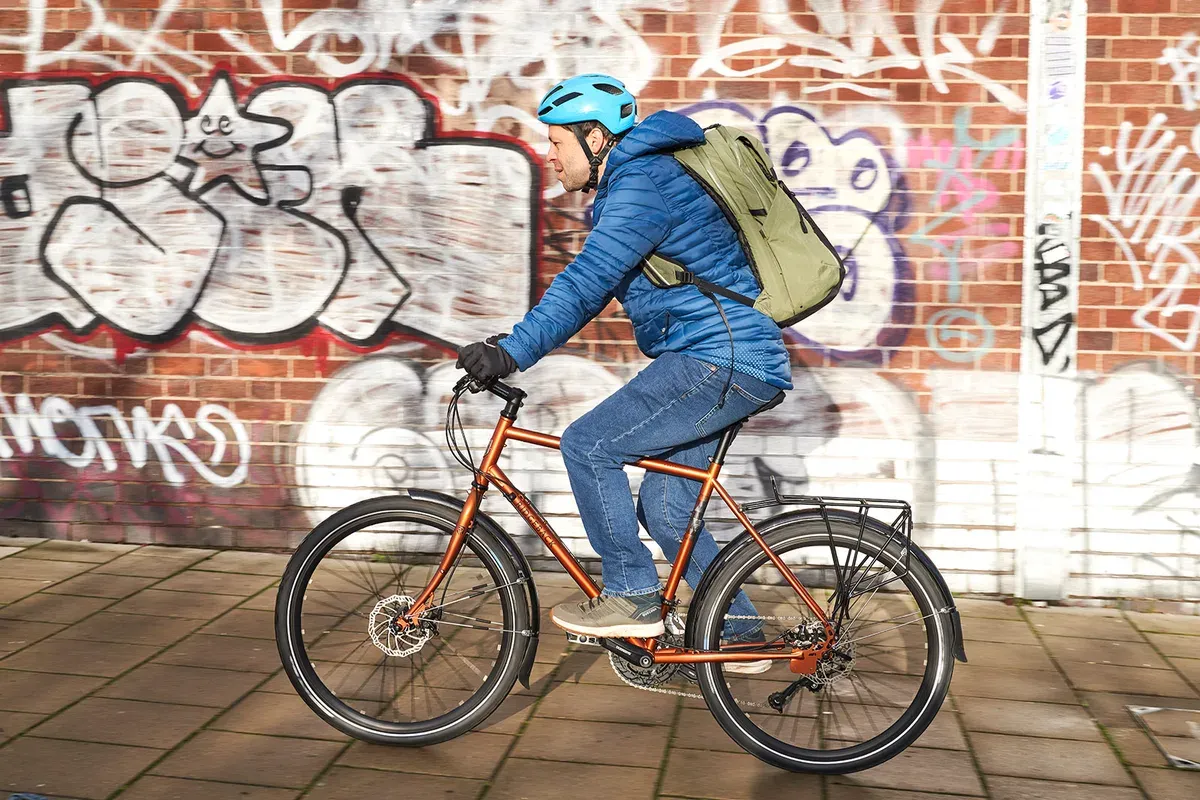 Orange Ridgeback bike, city bike frame, cyclist wearing a blue helmet, graffiti wall in the background
