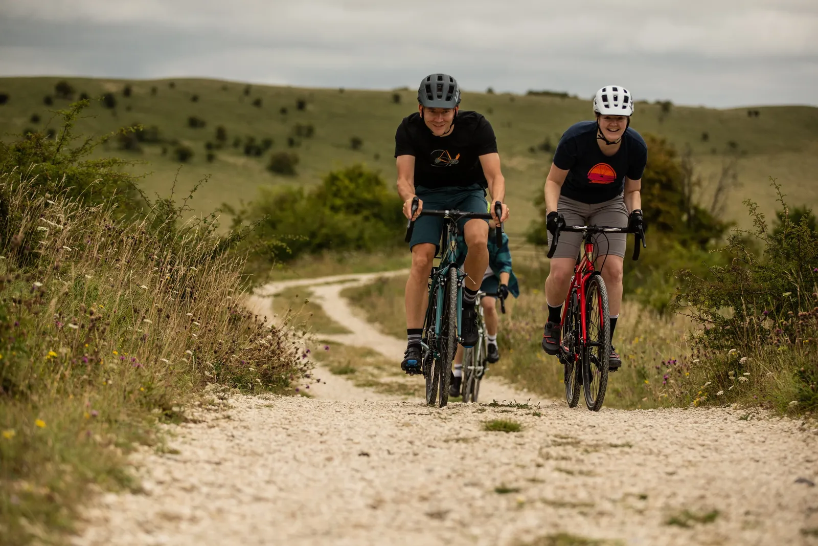 Two cyclists on Ridgeback bikes on a country road, with green hills in the background and a cloudy sky