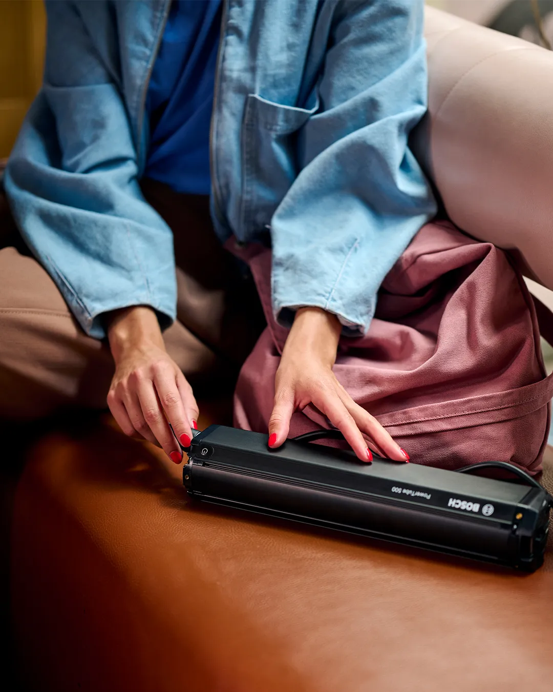 A person is charging a Bosch battery for a Batavus electric bike while sitting on a brown leather sofa