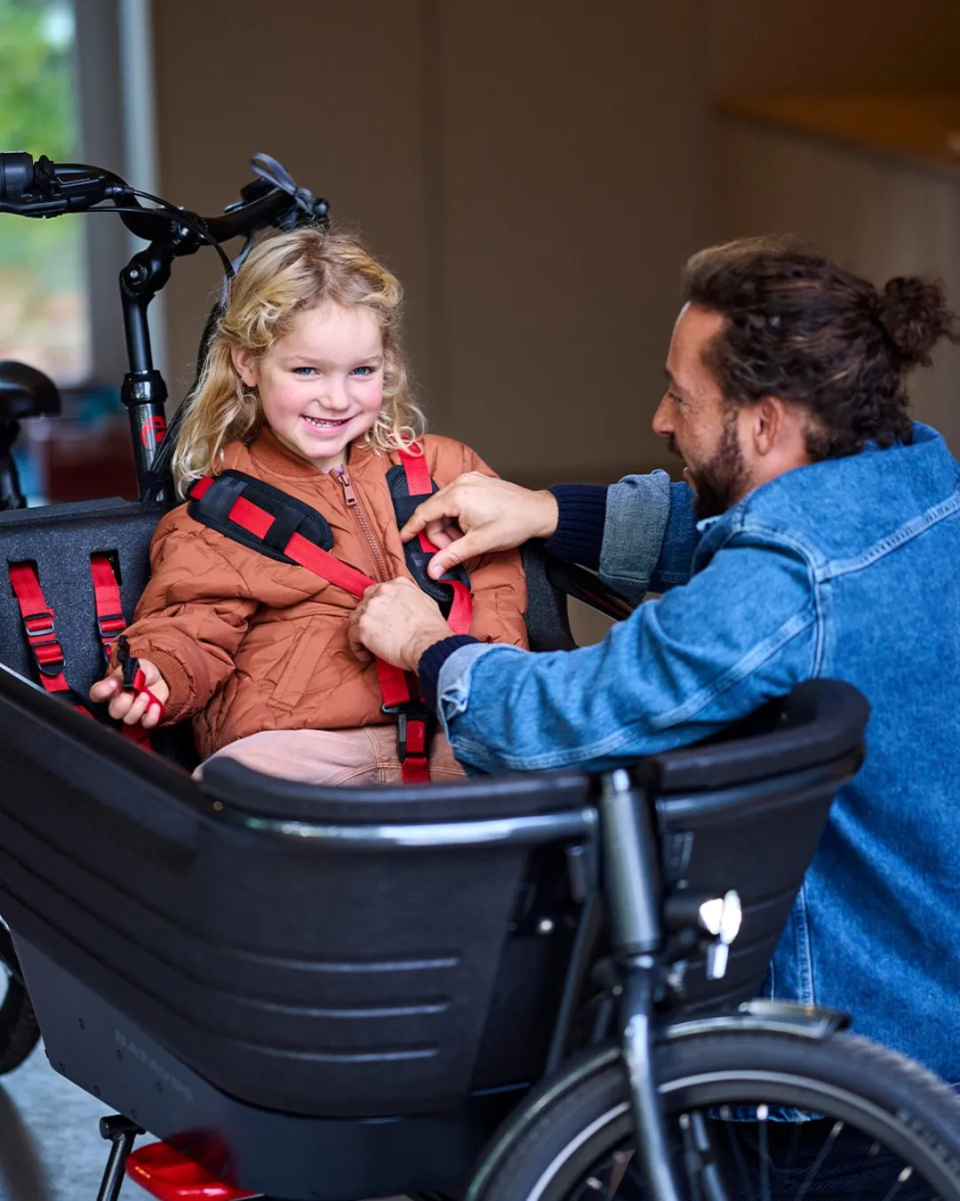 Black Batavus cargo bike with a child seated in the front, a man adjusting the straps