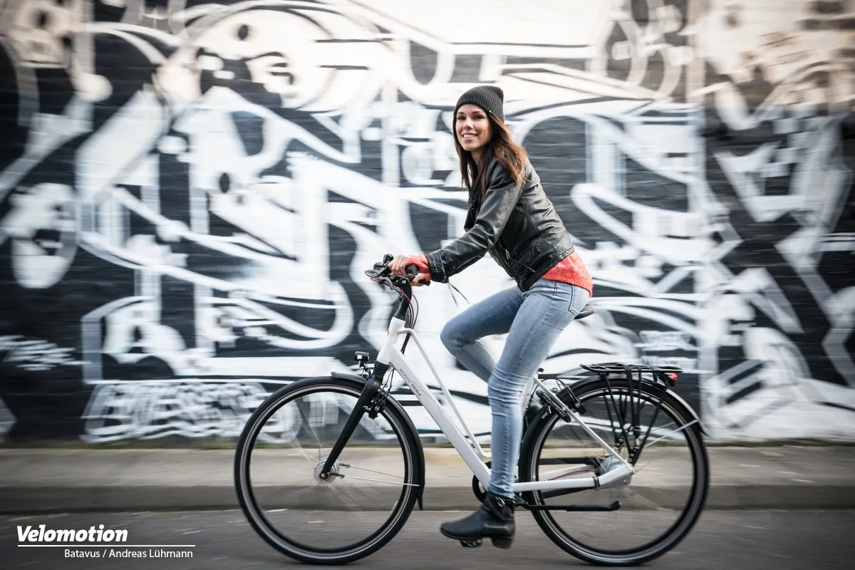 White Batavus bicycle with a straight frame, a smiling woman, and a graffiti wall in the background