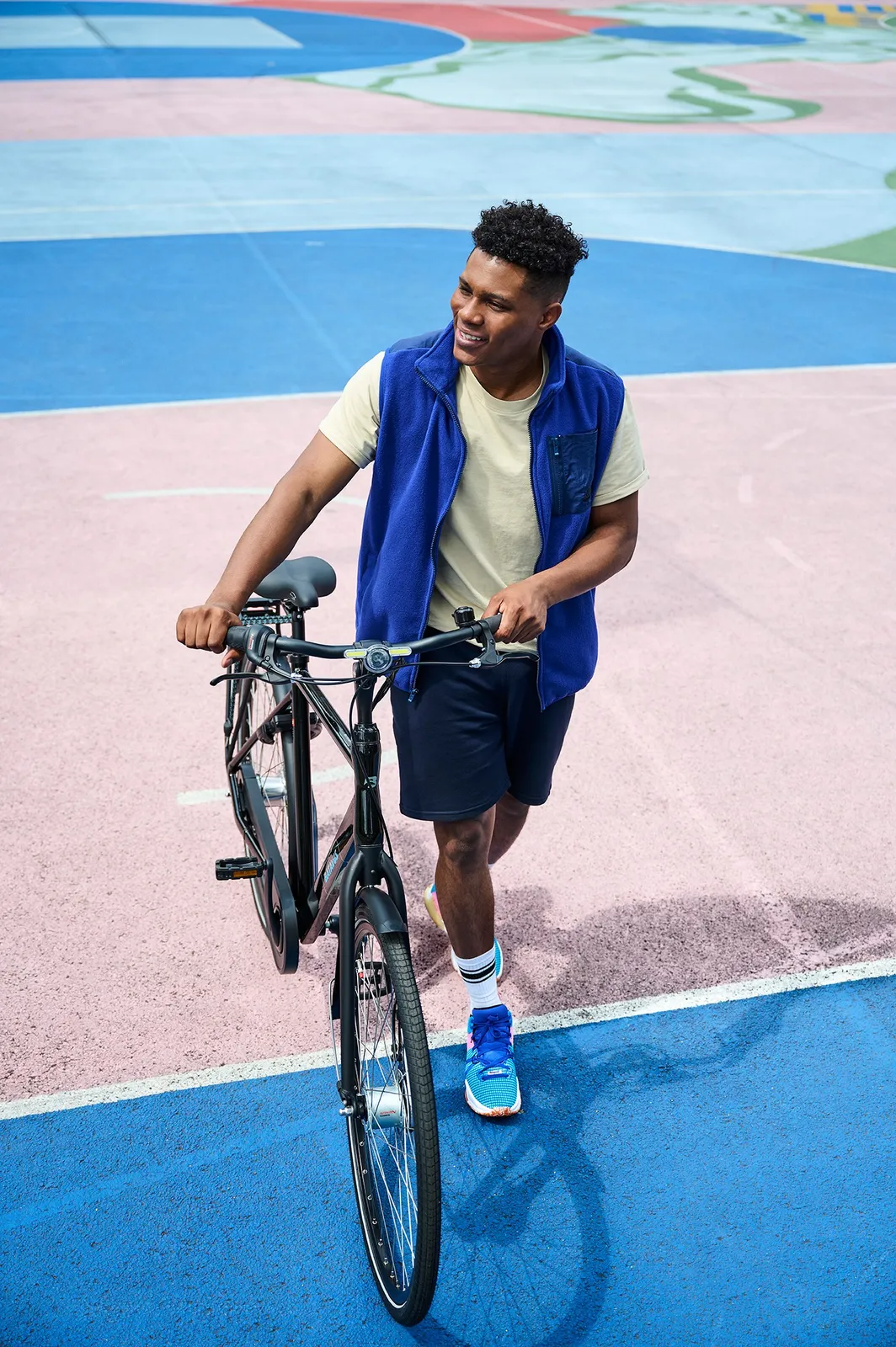 A black Batavus bicycle with an elegant frame on a colorful sports field, with a smiling man standing next to it