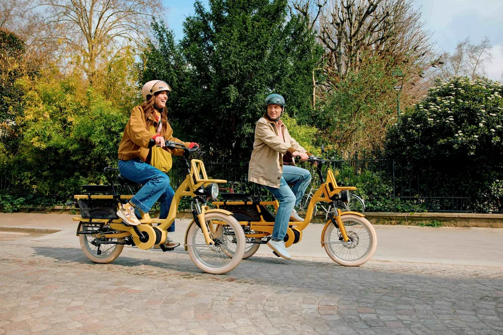 Deux cyclistes casqués sur des vélos longtail Gaya jaunes dans une allée de parc