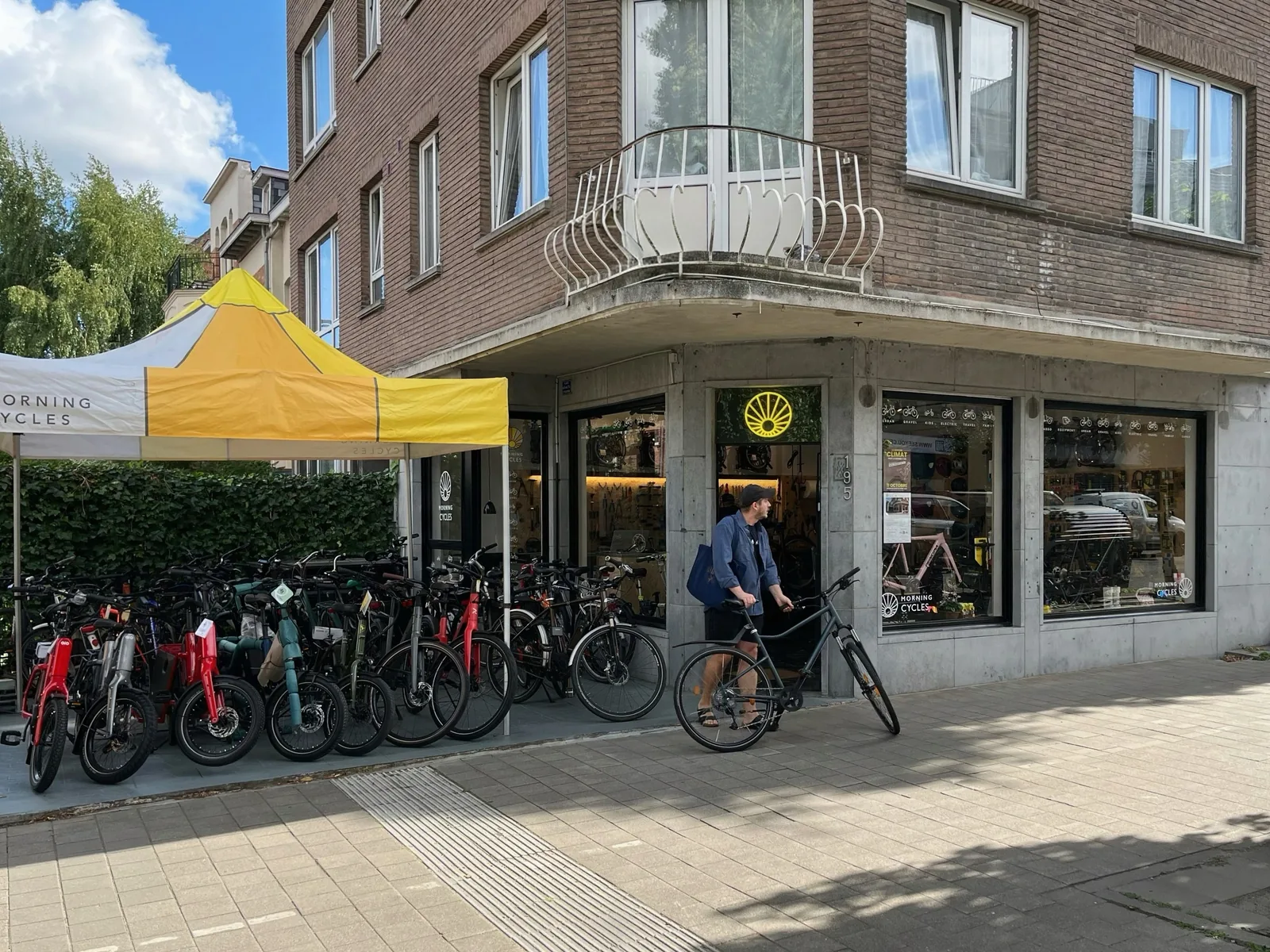 Magasin de vélos Morning Cycles avec une tente jaune et une sélection de vélos en exposition devant.