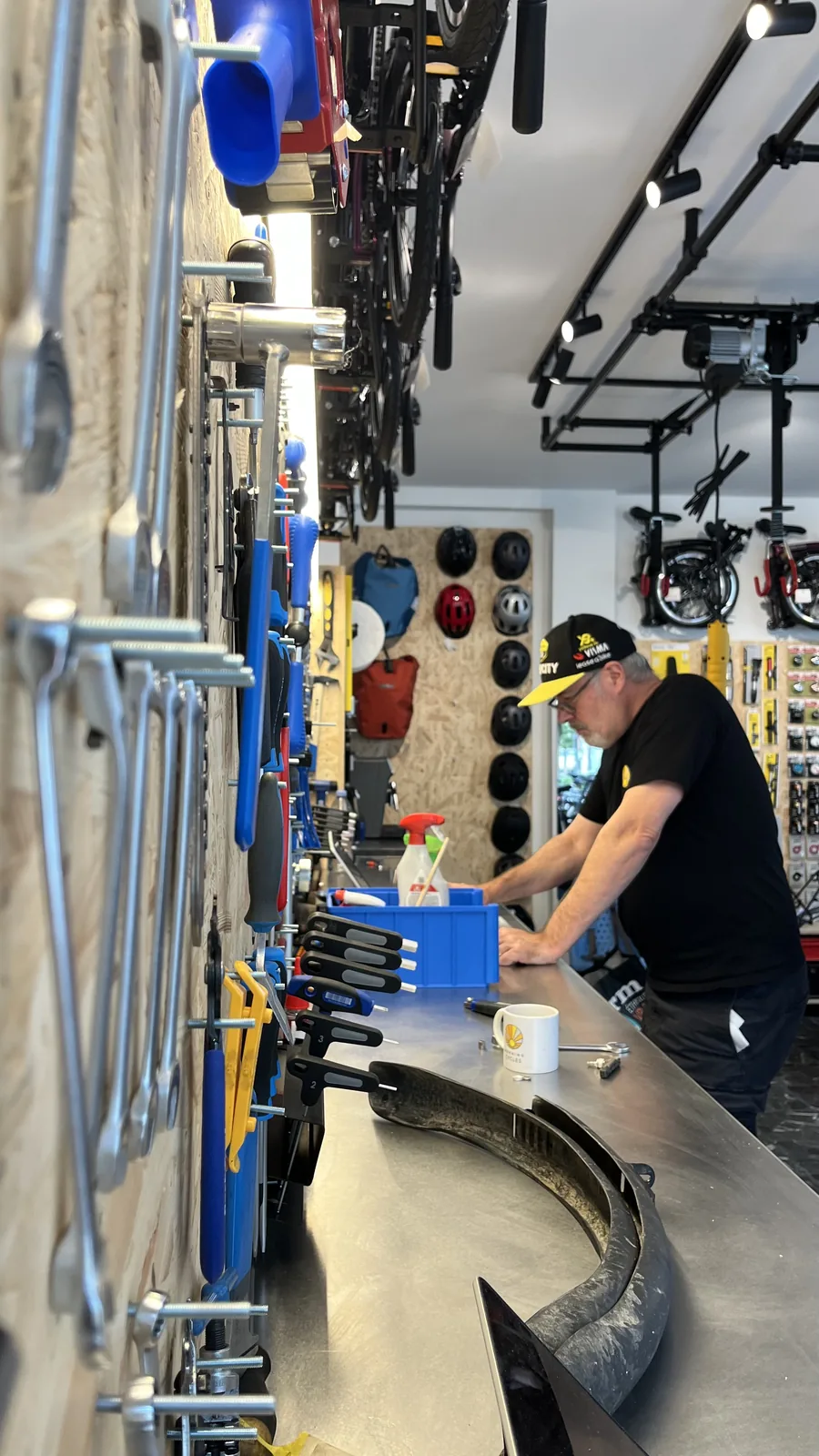 Un mécanicien travaille sur un vélo dans un atelier avec des outils suspendus au mur et divers équipements en arrière-plan.