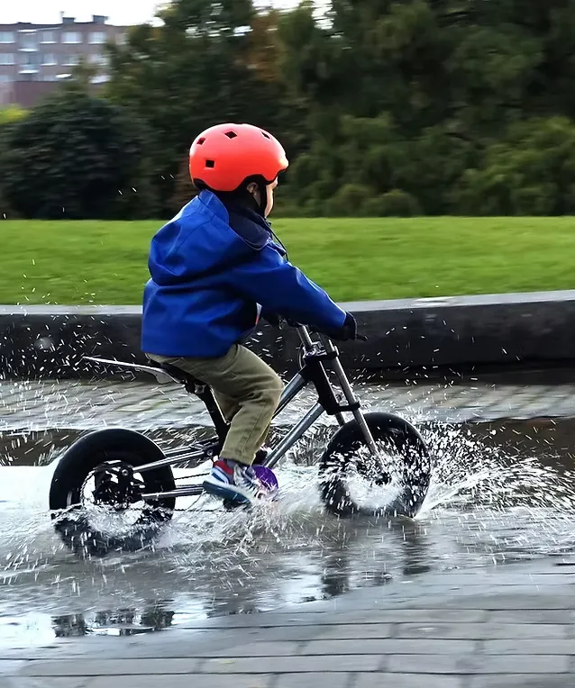 Enfant au casque orange roulant sur un vélo Bonob dans une flaque d'eau, dans un parc