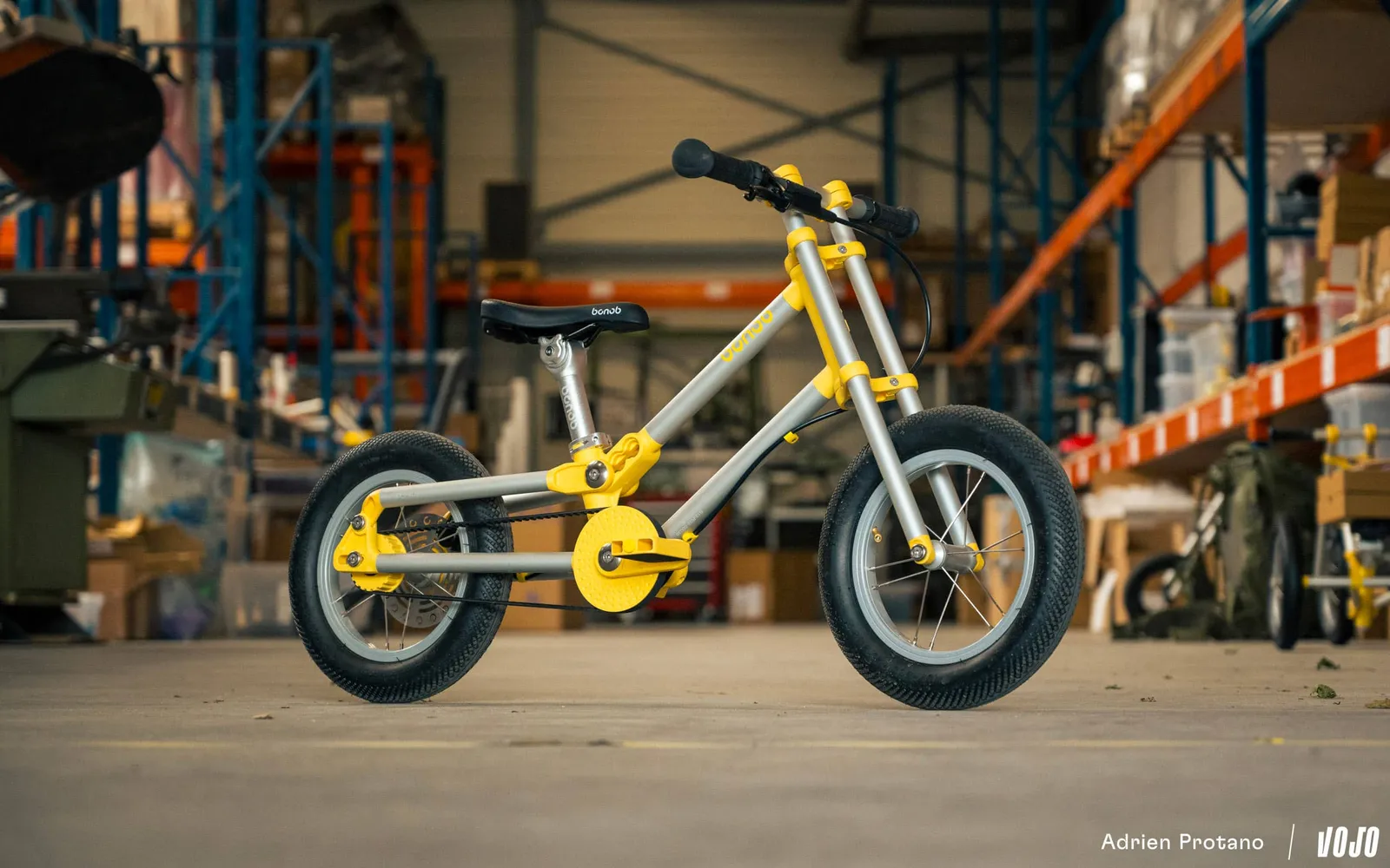 Vélo enfant Bonob jaune et aluminium en version vélo à pédales avec courroie, dans un entrepôt