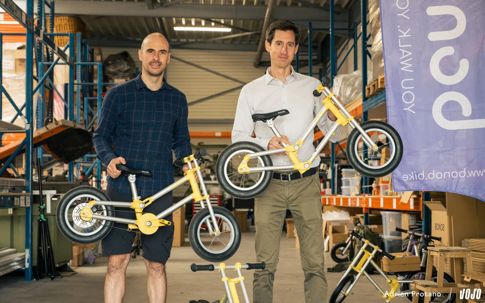 Les deux fondateurs de Bonob tenant des vélos enfant jaunes dans leur entrepôt