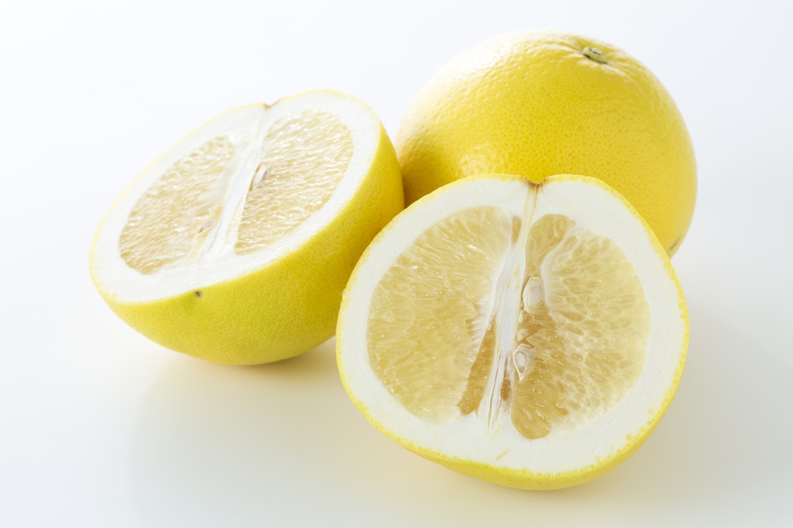 A whole yellow grapefruit next to another yellow grapefruit cut in half