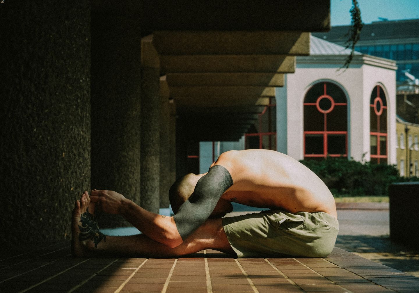 A tattooed Singaporean man reaching for his toes while sitting on the ground