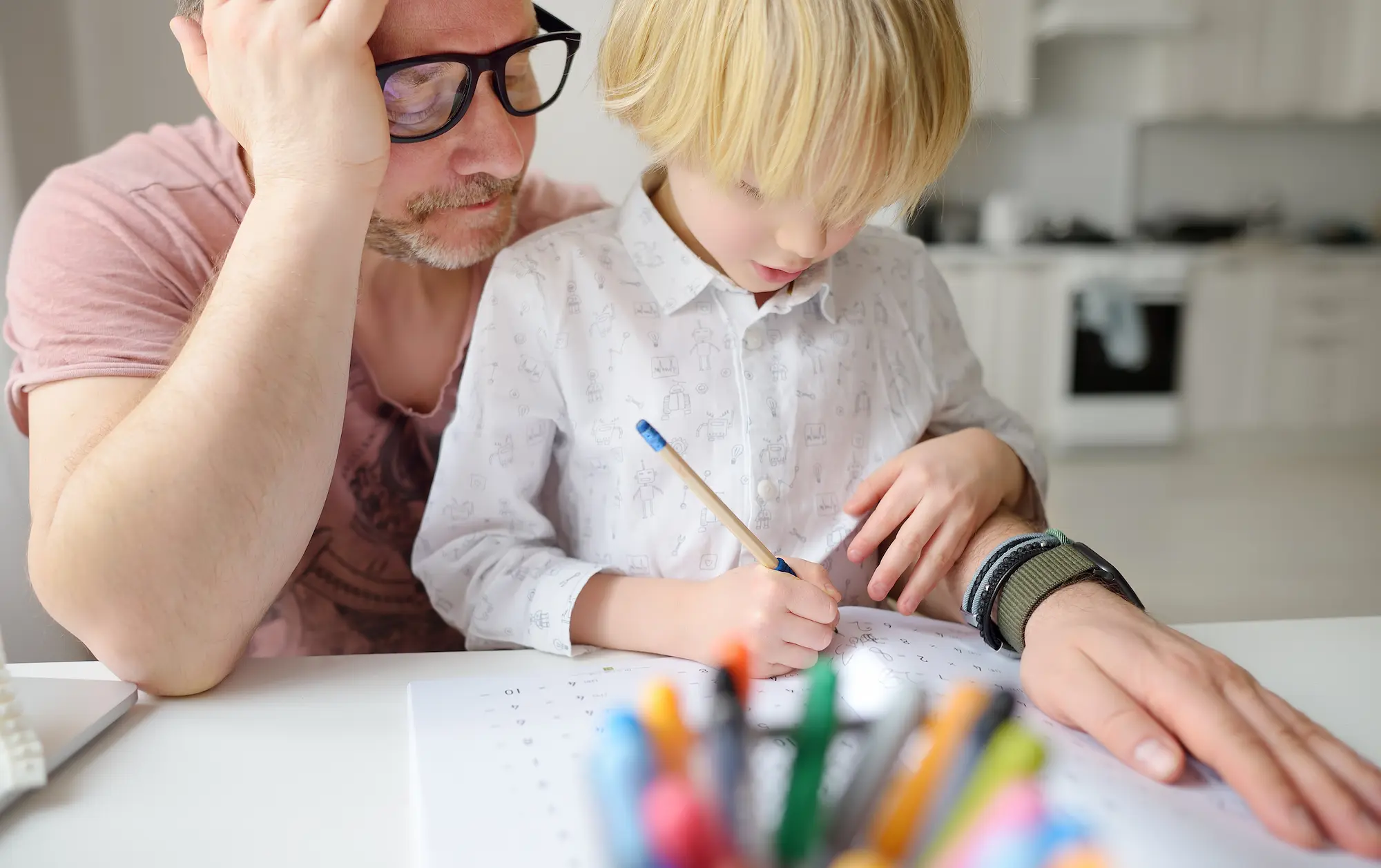 A parent helps their young child with schoolwork at the kitchen table.
