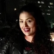 Smiling woman with curly hair wearing a dark jacket at night with building lights in the background.