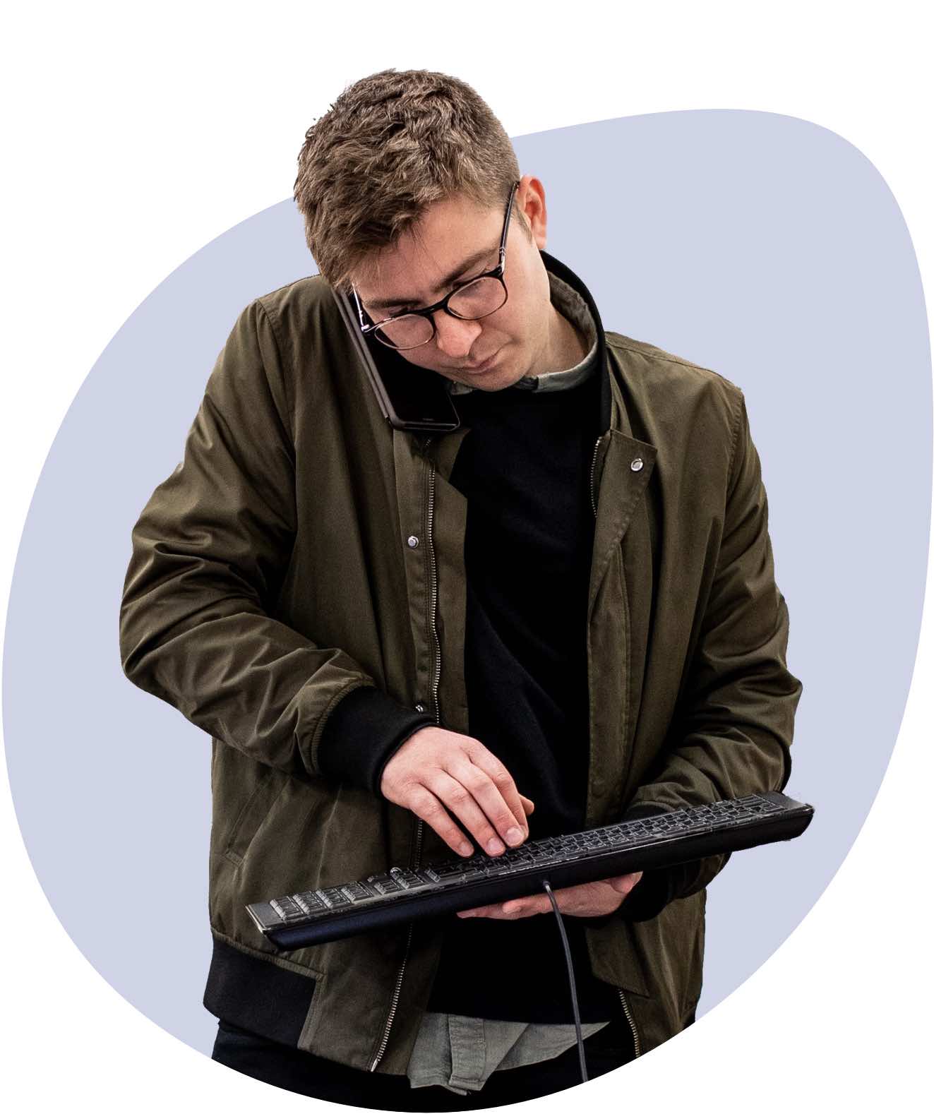 An Engineer standing, speaking on the phone while typing into a keyboard.