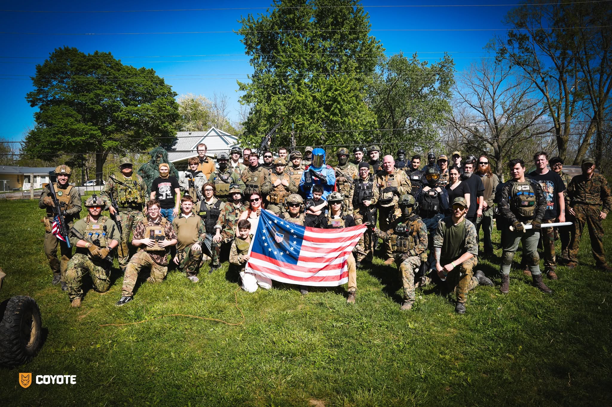 Large Coyote Force community group photo with flag at an outdoor event