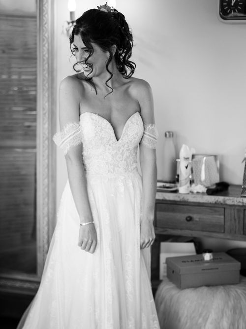 Smiling bride in a strapless lace wedding gown looking to the side indoors.