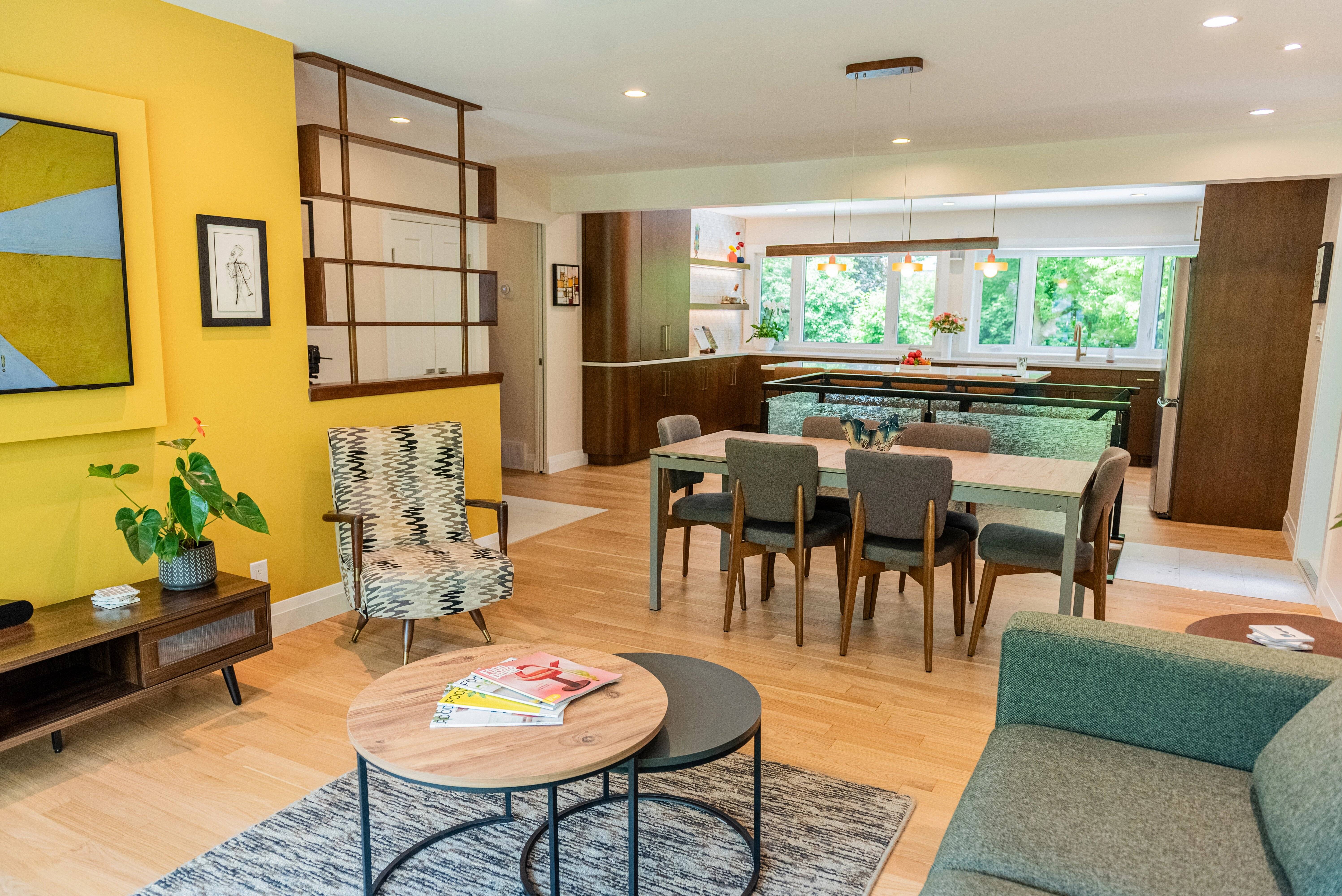 Mid-century modern open-concept living room with a yellow accent wall and an open kitchen layout. 