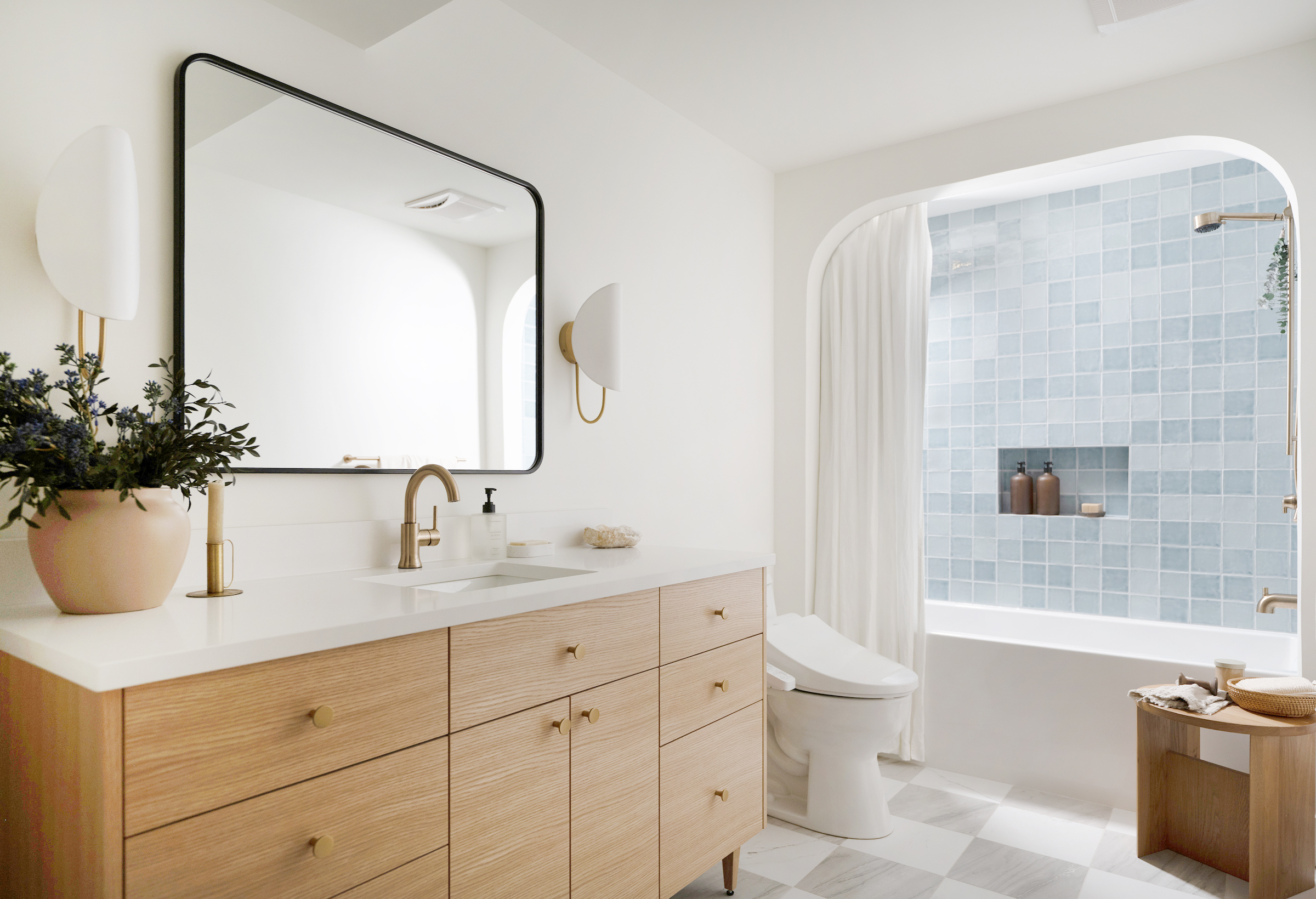 Bathroom vanity with warm wood cabinetry, square black-framed mirror, and blue accent tile in the walk-in shower