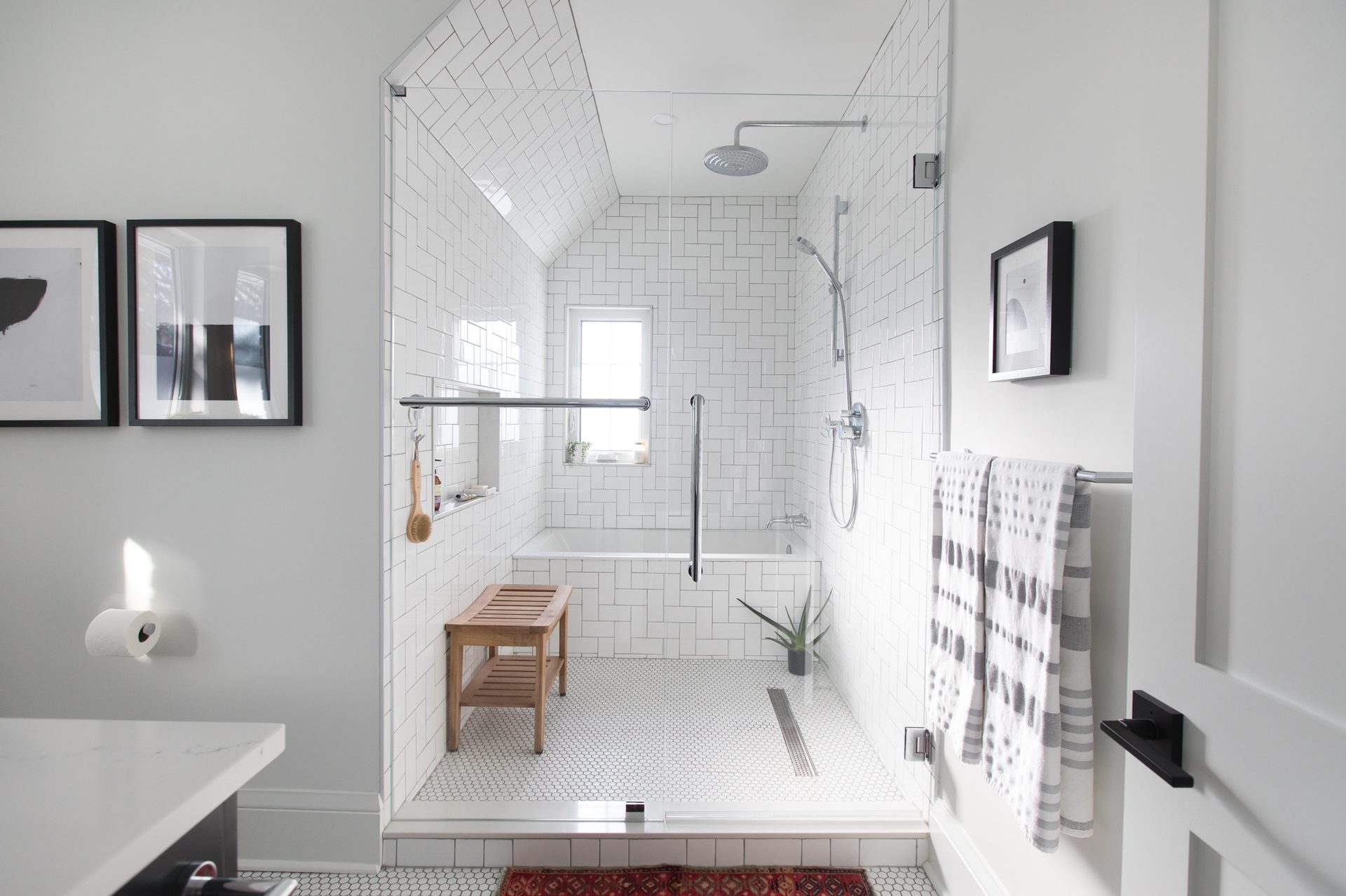 A white tiled walk-in shower with a wood bench in an Eagleview Construction Westmount bathroom renovation