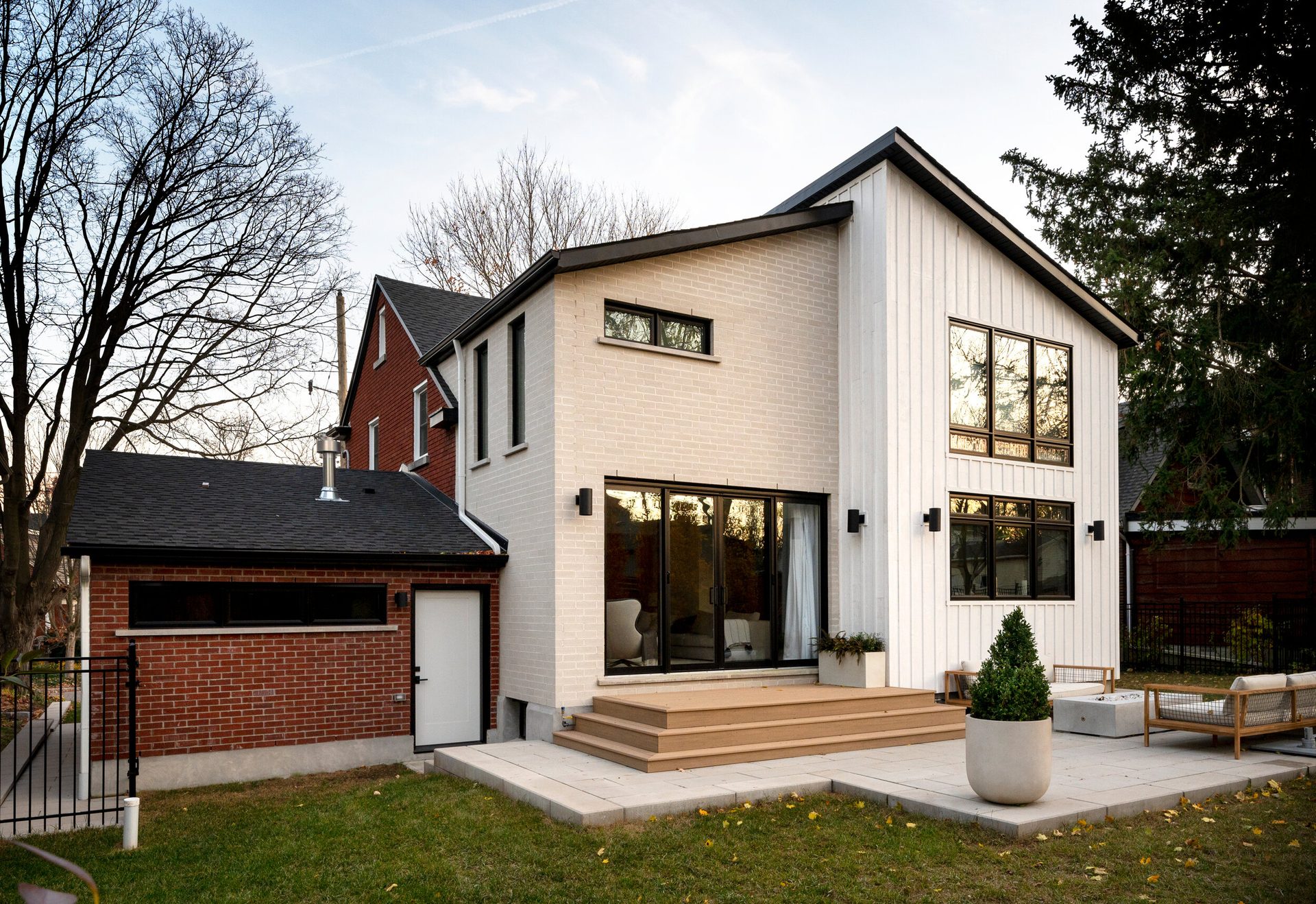 Rear exterior of a Westmount home addition with white brick, board-and-batten siding, and a wood deck