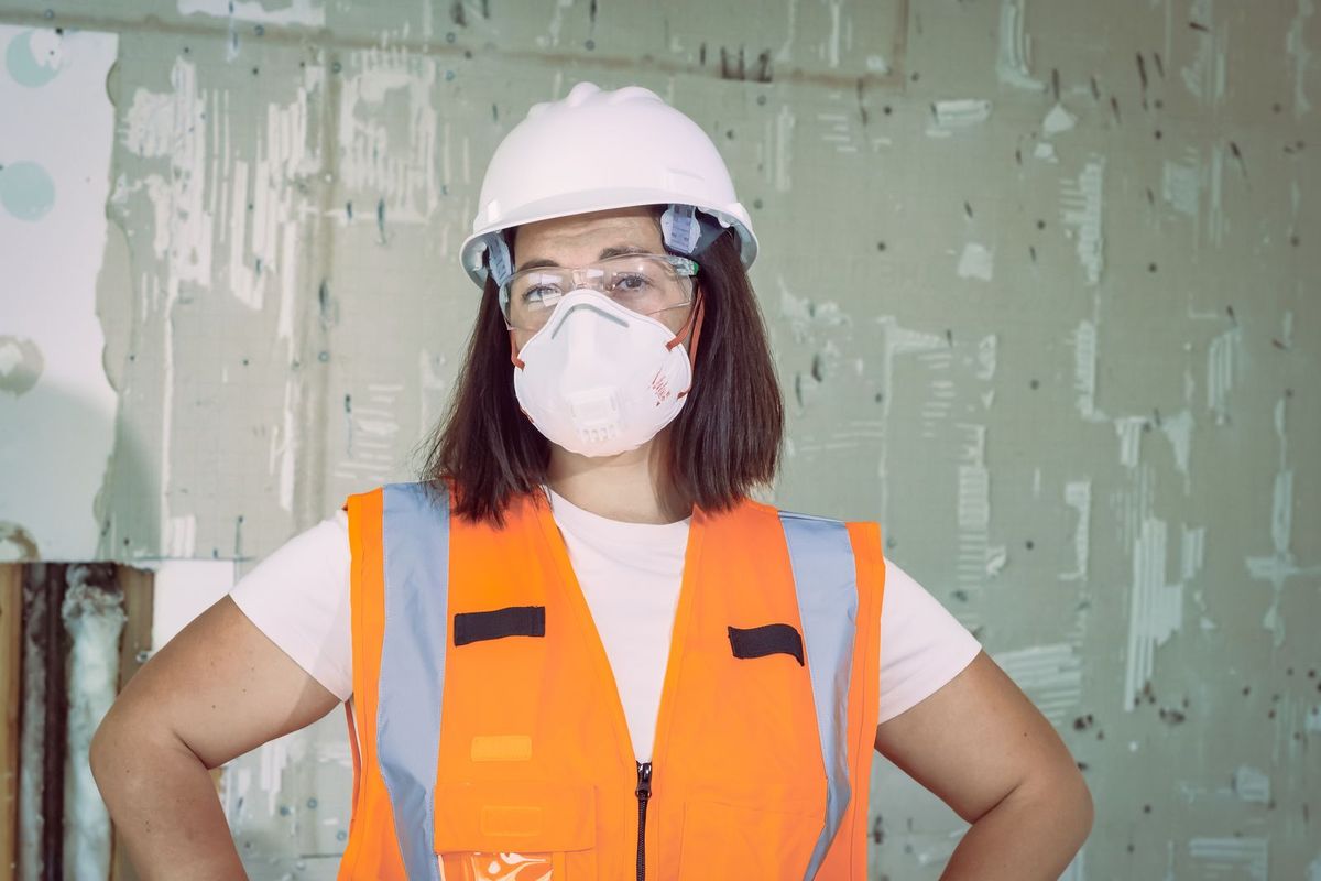 Renovation professional wearing a hard hat, safety glasses, N95 mask and safety vest in a room being prepared for renovation