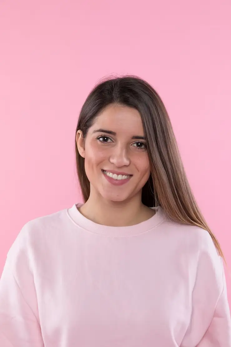 A cute girl smiling with long brown hair in a light pink background