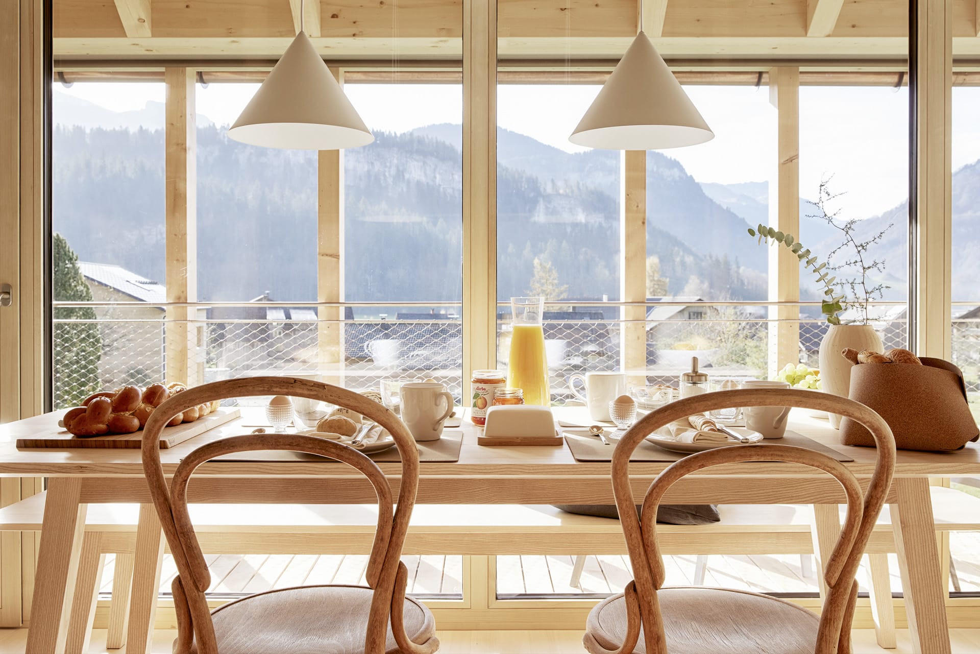 Gedeckter Frühstückstisch mit frischem Gebäck, Frühstückseier, Kaffee in sonnendurchfluteter Küche mit Blick auf die Berge in der Umgebung.