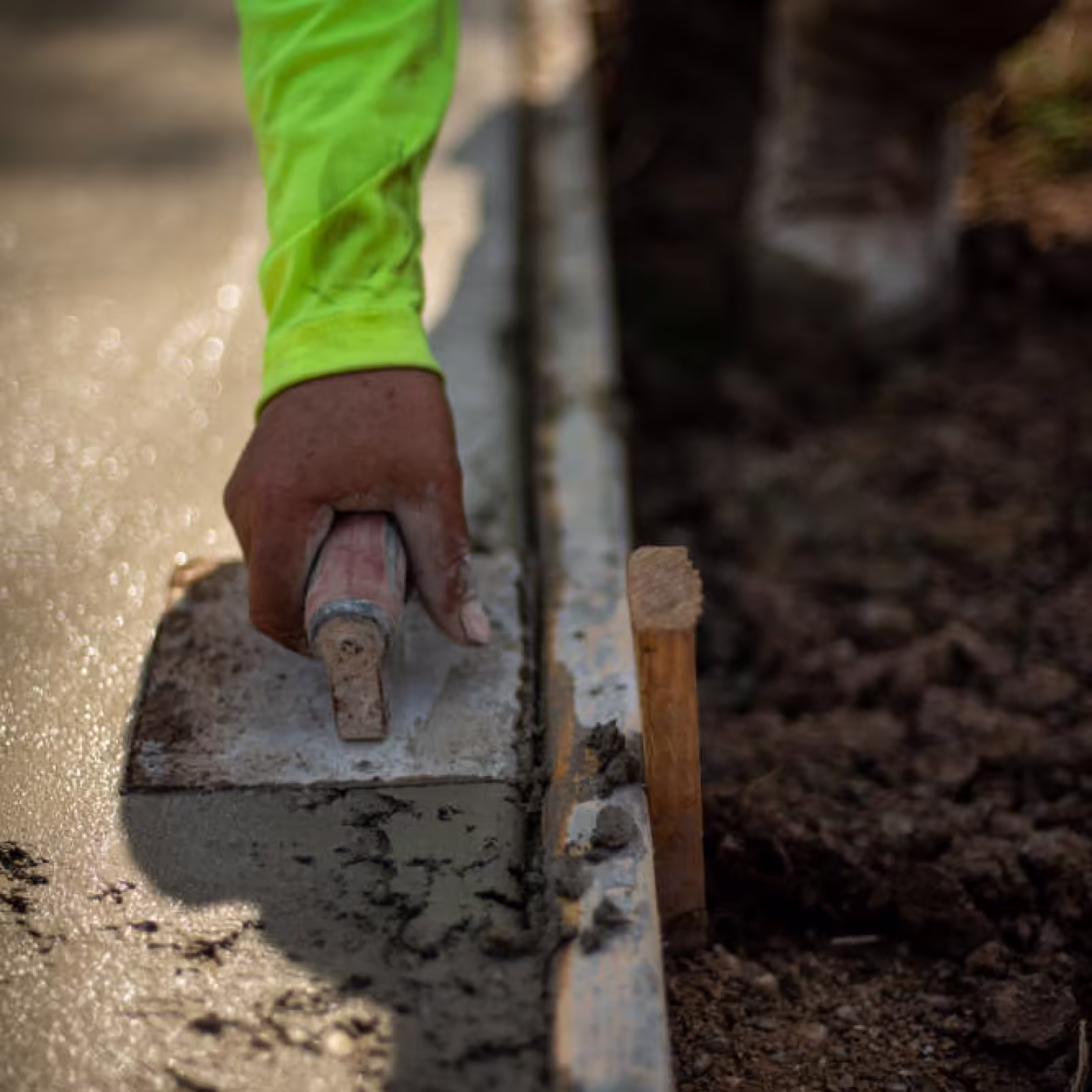 Concrete finisher hand-edging fresh concrete slab along form board on a Pro Concrete Services job site