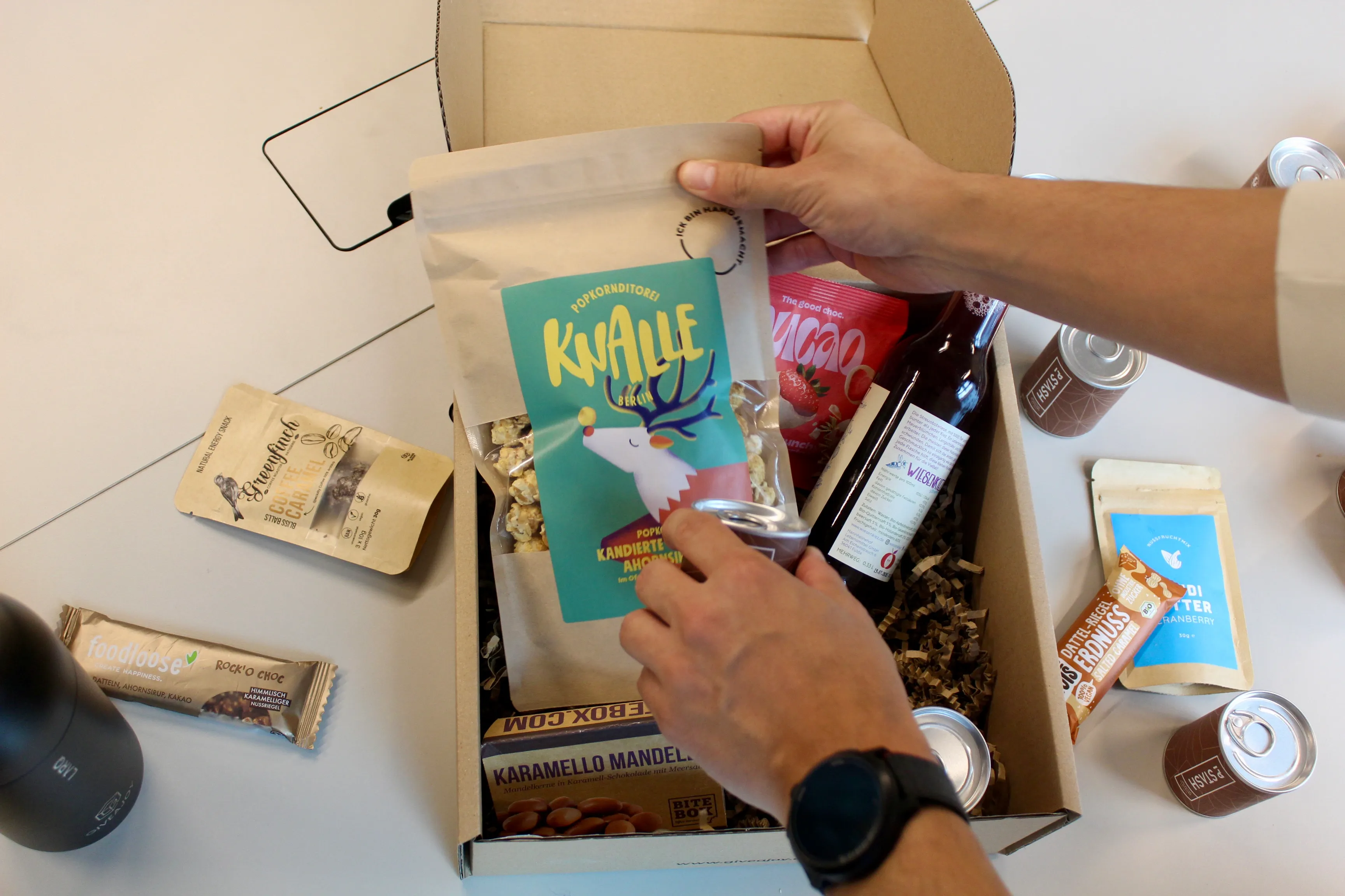 Person packt regionale Geschenkbox mit innovativen Start-up Produkten aus Berlin – hochwertige Mitarbeitergeschenke von GIVEAJOY mit Popcorn, Snacks, Getränken und nachhaltigen Leckereien.