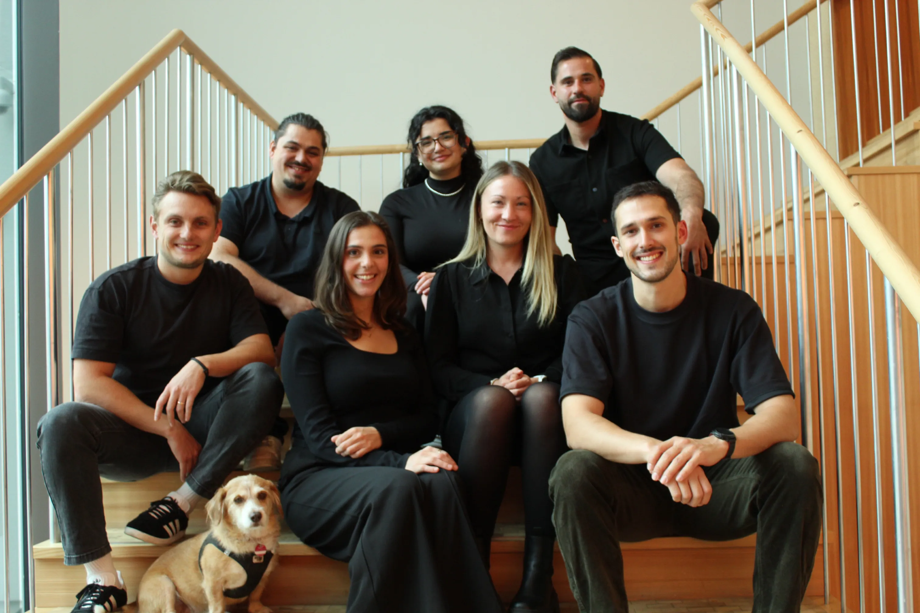 Das Team von GIVEAJOY aus Berlin sitzt gemeinsam auf einer Treppe – engagierte Mitarbeiter:innen eines Start-ups für nachhaltige und regionale Geschenkboxen für Unternehmen und Mitarbeitergeschenke.
